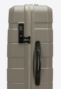 Valigia rigida di colore grigio chiaro con finitura testurizzata, dotata di una combinazione di lucchetto, chiusura a zip e maniglia nera.