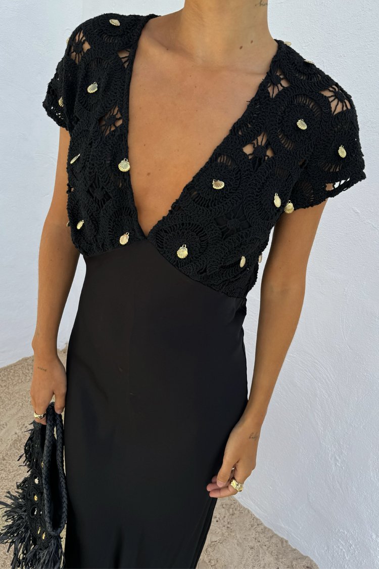 Schwarzes Häkeloberteil mit kurzen Ärmeln, das runde Muster und goldene Metallakzente aufweist, kombiniert mit einem taillierten schwarzen Kleid.