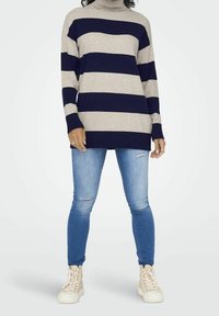 Gestreifter Rollkragenpullover in Hellgrau und Marineblau, kombiniert mit hellblauen, zerrissenen Skinny-Jeans und weißen High-Top-Sneakern.