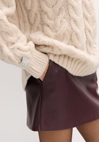 Kremowy sweter o grubym splocie z prążkowanym wykończeniem i detalem z metką w połączeniu z bordową mini spódnicą ze skóry z bocznym rozcięciem.