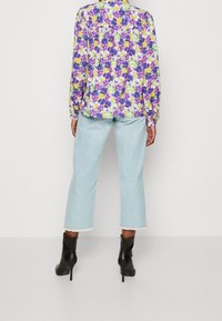 Blouse florale en violet, jaune et vert sur fond blanc ; jeans courts bleu clair avec ourlet effiloché ; bottines noires.