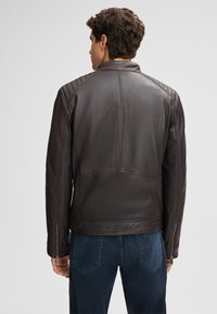 Braune Lederjacke mit gesteppten Schulterakzenten und tailliertem Design. Verfügt über einen Stehkragen und Reißverschlusstaschen an den Seiten.