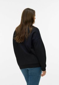 Svart genser med ledig passform, ribbede mansjetter og nederkant, og myk tekstur. Kombinert med blå jeans, sett bakfra.