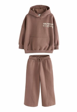 Brauner Baumwollhoodie mit großer Fronttasche und weißem Textdesign, kombiniert mit passenden weiten Hosen mit elastischem Bund.
