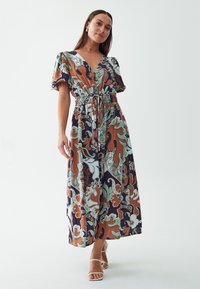 Robe maxi avec un décolleté en V profond, des manches courtes et une taille élastique. Présente un motif floral abstrait multicolore sur un fond sombre.