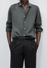 Dark green button-up shirt with long sleeves, roll-up cuffs, and white buttons, paired with black trousers and a black belt.