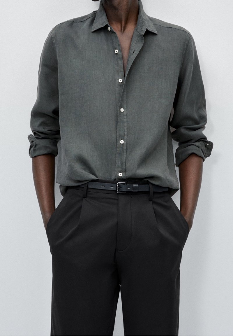 Dark green button-up shirt with long sleeves, roll-up cuffs, and white buttons, paired with black trousers and a black belt.