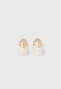 Baskets blanches à texture lisse, avec un accent doré sur le talon. Design minimaliste avec une semelle plate et un logo au dos.