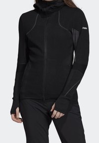 Veste zippée noire à manches longues en tissu texturé, col montant et passe-pouces. Présente un design à panneaux contrastés et une coupe ergonomique.