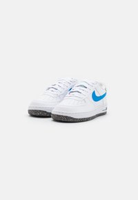 Białe sneakersy z niebieskim logo Swoosh. Posiadają perforowany czubek dla wentylacji oraz teksturowaną czarną podeszwę z recyklingu z kolorowymi drobinkami.
