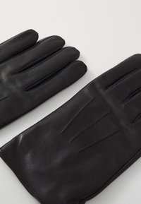 Guantes de cuero negro con una textura suave, que cuentan con cinco dedos alargados y acentos de costura vertical en la parte posterior.