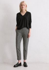 Lockerer schwarzer V-Ausschnitt-Pullover, graue gemusterte, schmal zulaufende Hose und schwarze Loafers. Einfaches Design mit weichem Material, geeignet für legere Anlässe.