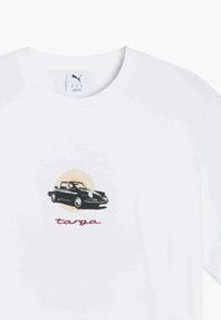 Hvid t-shirt med et sort bilgrafik på en cirkulær beige baggrund, ledsaget af teksten "tanga" i rød kursiv skrift.