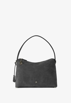 Grijze suède handtas met een gebogen silhouet, enkele schouderband, hardware in goudkleur en een ritssluiting. Textuurdetails zichtbaar op het oppervlak.