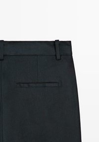 Zwarte, op maat gemaakte broek met een achterzak met paspel en riemlussen op een witte achtergrond.