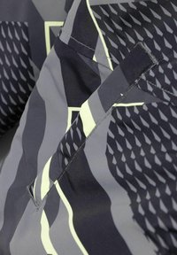 Tessuto della giacca grigia con motivi geometrici e dettagli testurizzati. I dettagli delle tasche cucite e le linee più chiare in contrasto arricchiscono il suo design.