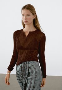 Donkerbruin, geribbeld langarmtop met een henleyhalslijn, gecombineerd met lichtblauwe en grijze stoffen broeken met een gemêleerd design en textuur.