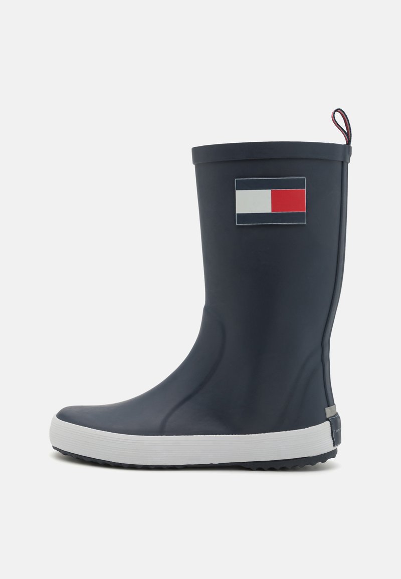 Botte de pluie en caoutchouc marine avec semelle blanche, arborant un logo rectangulaire en rouge, blanc et bleu sur le côté extérieur. Surfaces texturées pour une meilleure adhérence.
