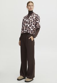 En cropped bluse med leopardmønster i brune og pink nuancer. Langærmet brun turtleneck under; brede brune bukser. Beige fodtøj.