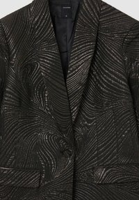 Schwarzer Blazer mit strukturierten Wirbeln, ausgestattet mit einem strukturierten Revers, einem Knopfverschluss und zwei vorderen Taschen. Gefüttertes Innere.