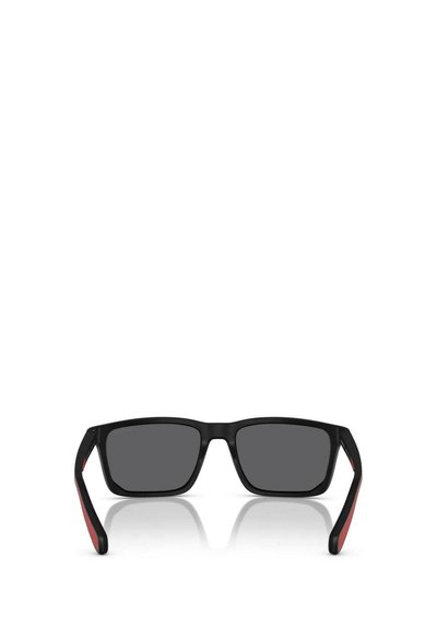 Lunettes de soleil noires avec une monture rectangulaire, des verres gris et des accents rouges sur les tempes. Finition mate texturée sur la monture.
