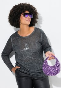 Maglietta grigia a maniche lunghe con design a stella in paillettes, abbinata a pantaloni neri lucidi e una borsa a tracolla viola in paillettes. Tessuto testurizzato e dettagli lucidi.