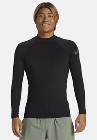 Rash guard negro de manga larga hecho de material elástico con cuello redondo y costuras planas; presenta un pequeño logo gris en el hombro izquierdo superior.