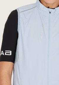 Lysblå ærmeløs jakke med en sort kortærmet basislag. Har en frontlynlås, åndbare mesh-sider og reflekterende detaljer.