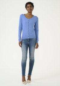 Lichtblauwe cardigan met lange mouwen en ronde halslijn, voorzien van knoopsluiting en geribbelde onderrand; gecombineerd met lichtblauwe skinny jeans.