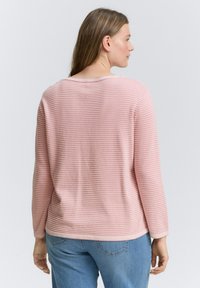 Hellrosa gestreiftes Langarmshirt mit Rundhalsausschnitt und gerippter Textur, kombiniert mit blauen Jeans; sichtbare Nahtdetails und lockere Passform.