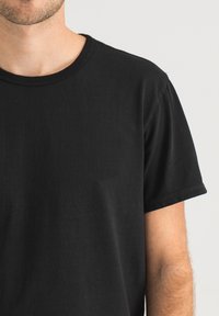 Schwarzes T-Shirt aus Baumwolle mit rundem Halsausschnitt und kurzen Ärmeln. Glatte Textur mit minimalen Nähten.