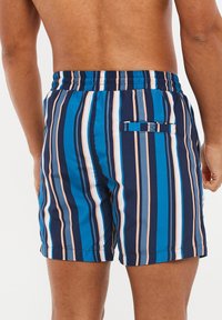 Bañadores de hombre en azul marino con rayas verticales de diferentes tonos de azul, rosa claro y gris. Cuenta con un bolsillo trasero con tapa.