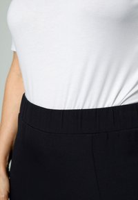 Svarta byxor med elastiskt midjeband som bärs tillsammans med en åtsittande vit t-shirt i bomull. Tyget verkar slätt med en lätt lyster.