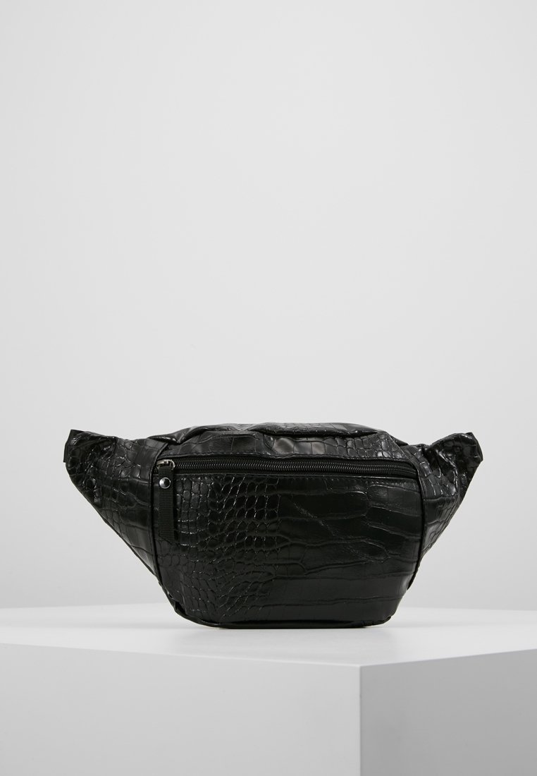 Sac banane en cuir noir embossé effet crocodile avec une poche avant zippée, présenté sur un socle blanc sur fond gris uni.