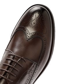 Chaussure oxford en cuir marron avec un design brogué décoratif, bout arrondi, fermeture à lacets et finition lisse et polie.