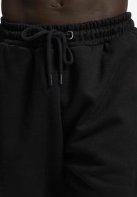 Black sweatpants made of soft fabric. Features an elastic waistband with drawstring and logo detail. Simple design with a smooth texture.