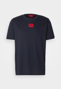 T-shirt en coton bleu marine à manches courtes, col rond, avec un patch carré rouge brodé portant le mot "HUGO" sur la poitrine.
