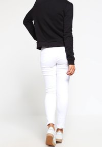 Sort cropped sweatshirt, hvide skinny jeans og lyse sneakers. Glat stof, tætsiddende design og rene linjer. Bagfra.