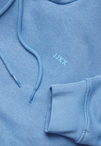 Light blue hoodie with a soft texture, featuring a kangaroo pocket, drawstrings, and "JJXX" logo in a matching light blue shade.
