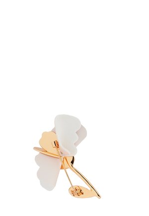 Broche i guldfarvet metal formet som en blomst med hvide bløde stofblade og en nålefæstning på bagsiden.
