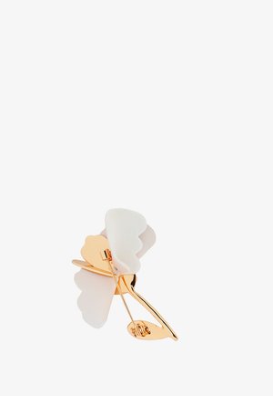 Broche i guldfarvet metal formet som en blomst med hvide bløde stofblade og en nålefæstning på bagsiden.