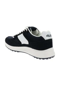 Zapatilla deportiva en blanco y negro con cordones blancos, detalles de malla y ante, y logo "4US" en el talón, vista desde un ángulo trasero lateral.