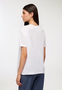 Biała koszulka z krótkim rękawem, wykonana z miękkiej bawełny, luźny krój, okrągły dekolt, z delikatnymi detalami szycia przy szwie ramienia.