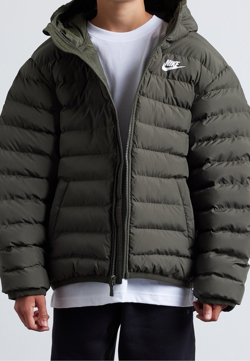 Grüne Daunenjacke mit gesteppter Oberfläche, Reißverschluss und Kapuze. Verfügt über ein kleines weißes Nike-Logo auf der linken Brust. Weicher Stoff.