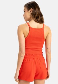 Röd rippad linne kombinerat med shorts med elastisk midja i matchande röd, som har två bakfickor och en designaccent på en ficka.