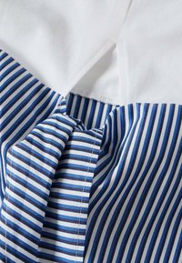 Camisa de algodón con rayas horizontales blancas y azules, con un tejido texturizado y un diseño plisado en la parte delantera para un detalle adicional.
