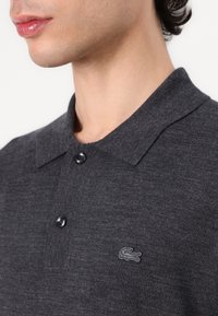 Czarny polo z ciemnoszarego materiału z teksturowej tkaniny, z klasycznym kołnierzykiem, dwiema guzikami i małym haftowanym logotypem na piersi.
