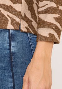Braun-beige Tiermuster-Pullover mit weicher Textur; hat einen lässigen Schnitt und umgeschlagene Ärmel, kombiniert mit blauen Denim-Jeans.