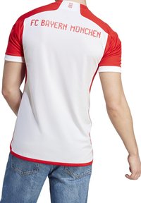 Punainen ja valkoinen FC Bayern München -paita, jossa on ribatty pinta, taustalla joukkueen nimi ja eriväriset hihasivua korostavat yksityiskohdat.