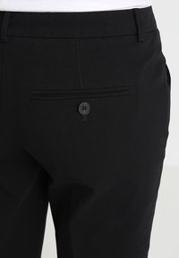 Pantalons noirs ajustés avec une texture lisse, un subtil éclat et une poche arrière boutonnée avec une élégante couture horizontale.